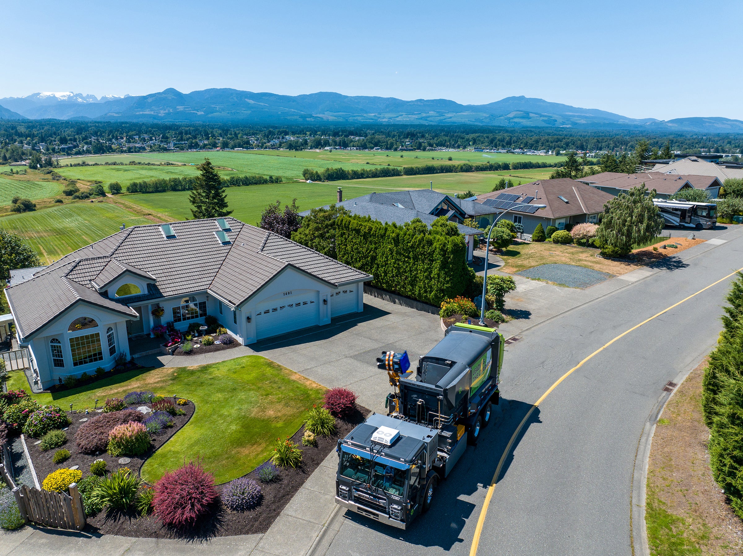 Electric truck: Emterra electric collection truck on a residential street with homes and mountains in the background.