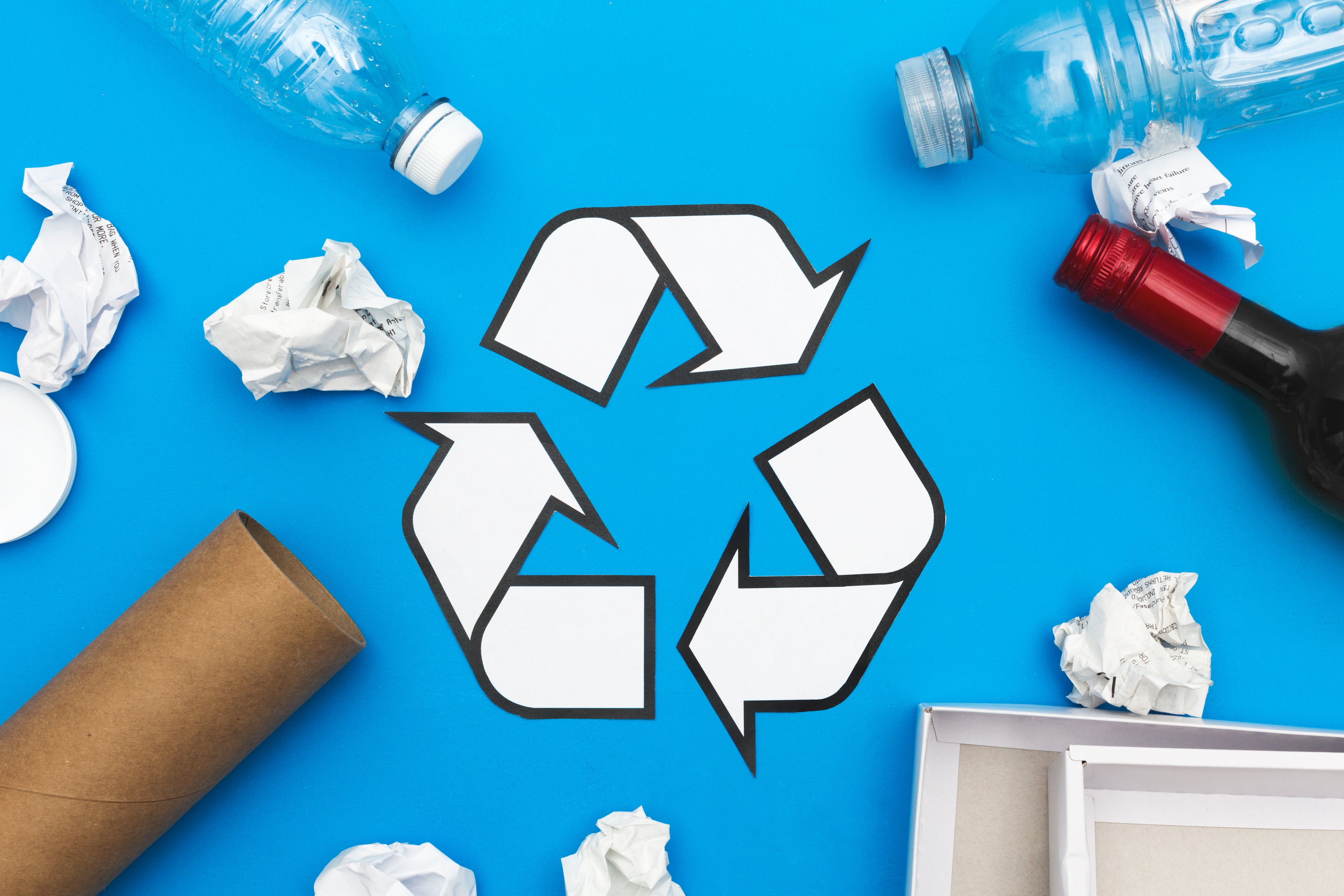 Recycle symbol: Recycling symbol on blue background with bottles, paper, cardboard tube, and packaging around it.